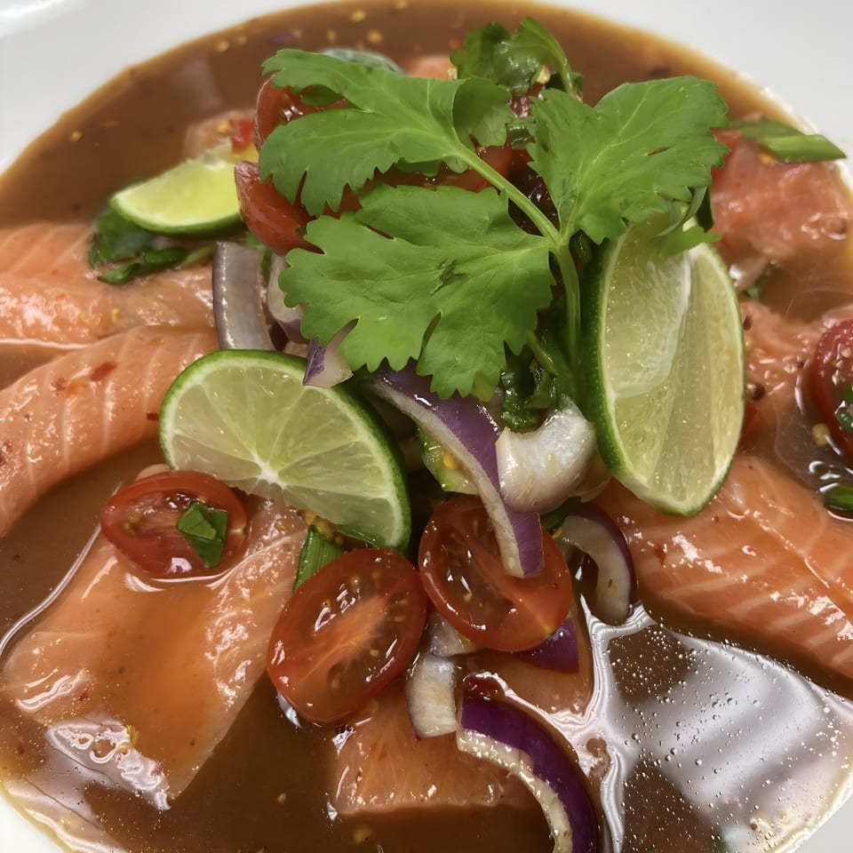 Thai salmon sashimi with lime, red onion, cherry tomatoes, and cilantro in a savory sauce.