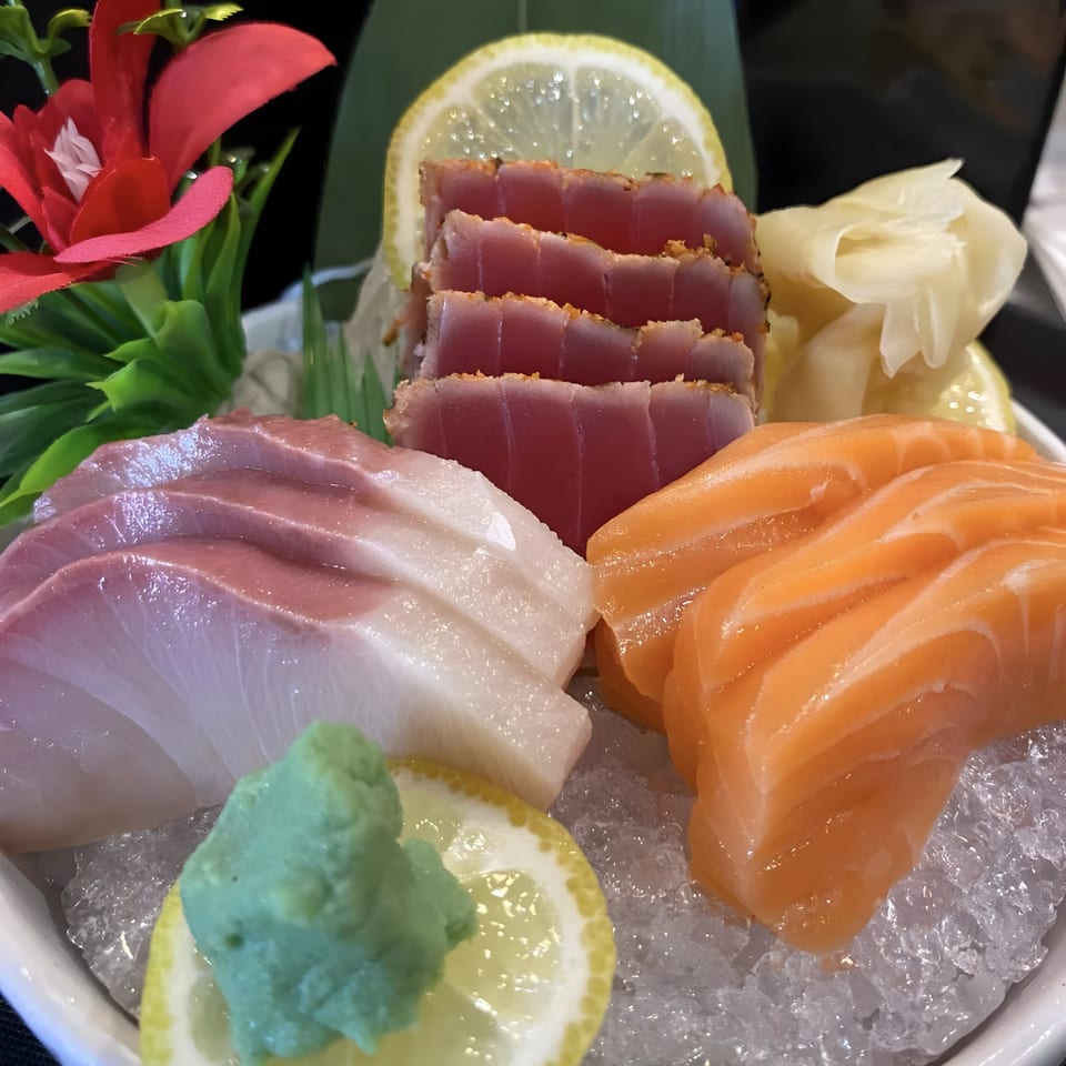 A platter of Thai Garlic & Sushi sashimi with tuna, salmon, and white fish on ice with lemon and wasabi.