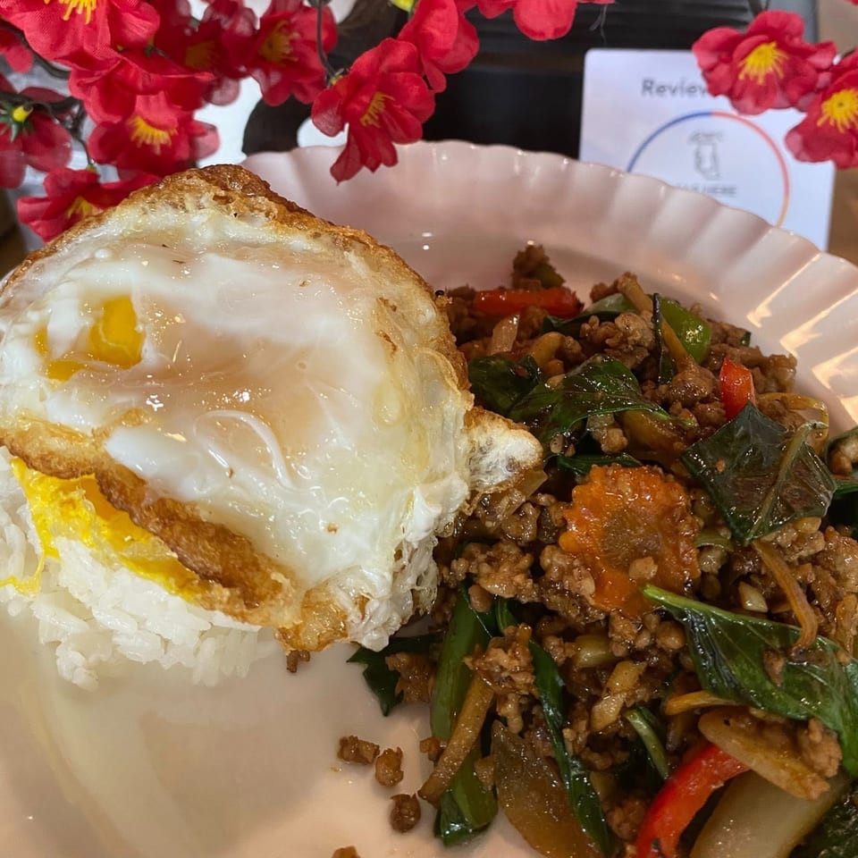Thai basil chicken with a fried egg and white rice, garnished with red flowers.