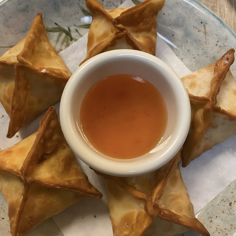 Crispy golden crab rangoons arranged around a small white bowl of sweet chili dipping sauce.