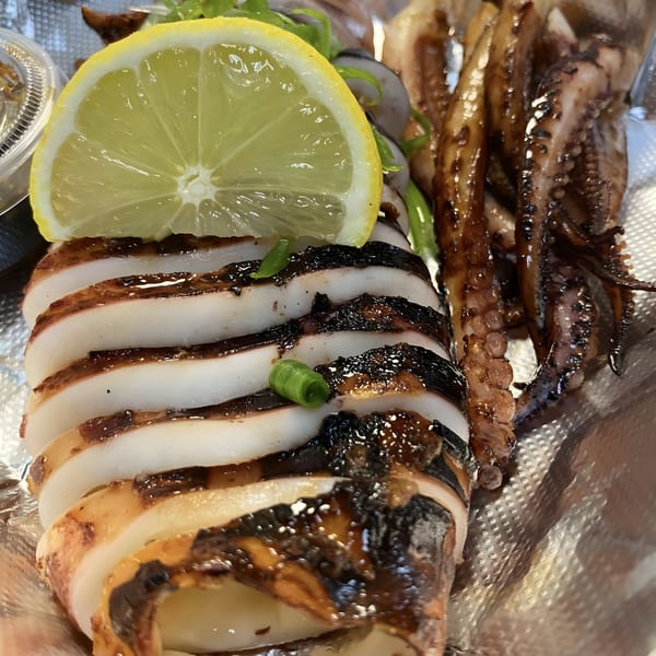 Grilled squid, sliced and whole, with a lemon wedge and green garnish on foil.