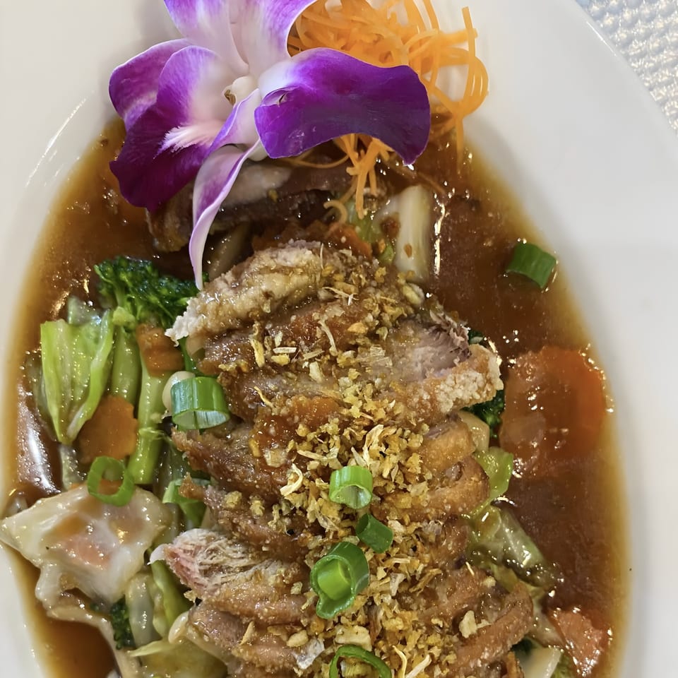 Crispy duck in brown sauce with mixed vegetables, topped with fried garlic and a purple orchid.