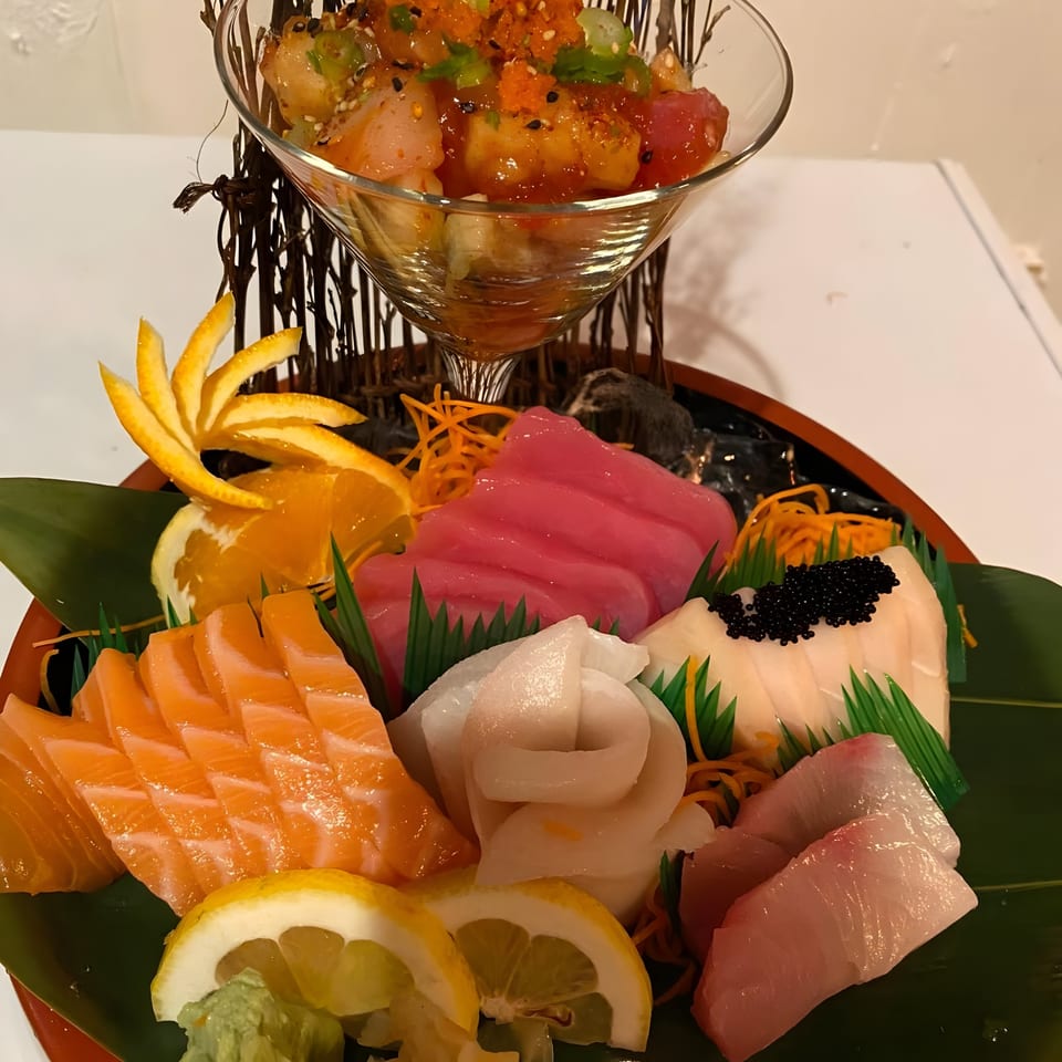 A colorful sashimi platter with salmon, tuna, white fish, and a martini glass of poke.
